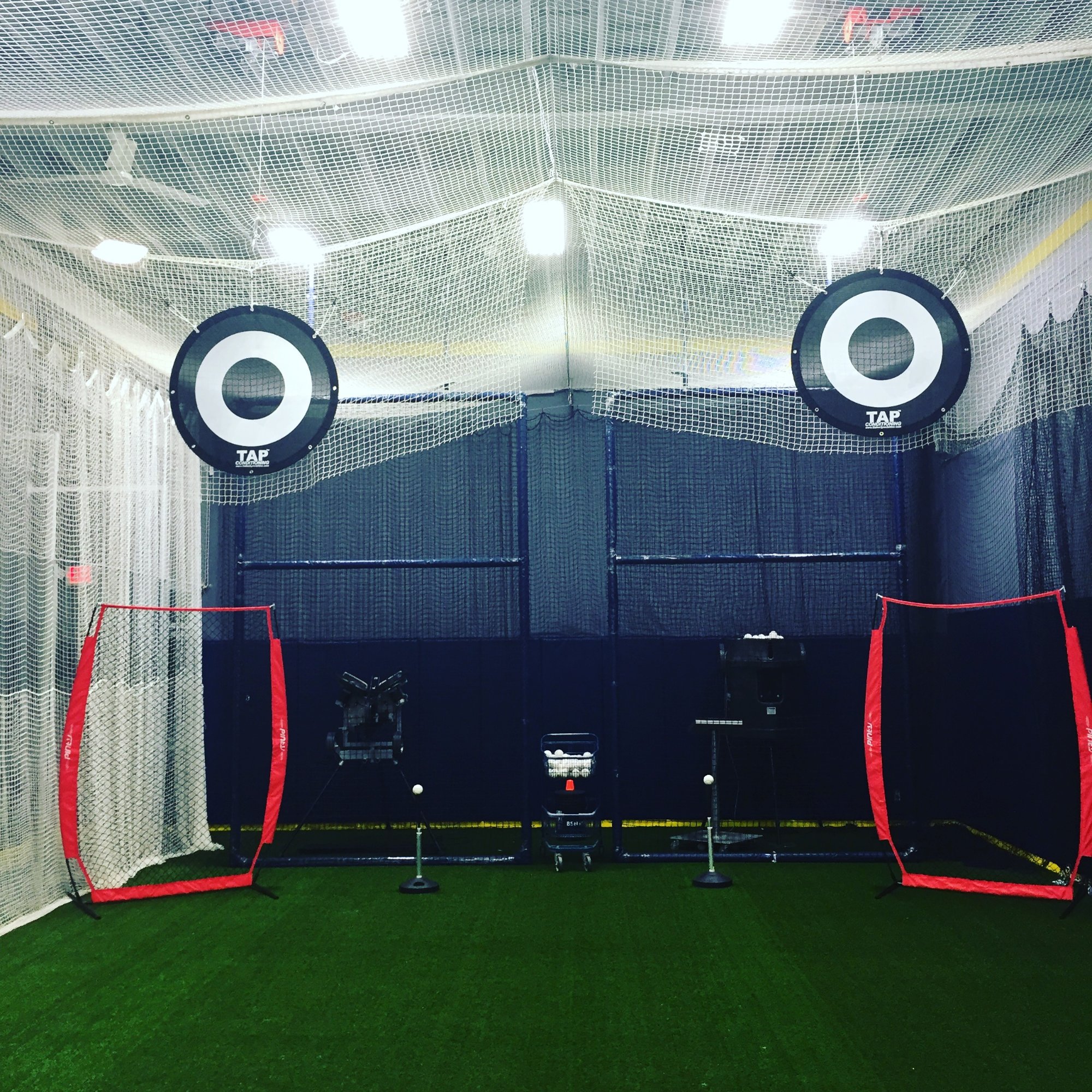 The turf arena at Saratoga Sports Club with batting cage nets, red L-screens and pitching machines