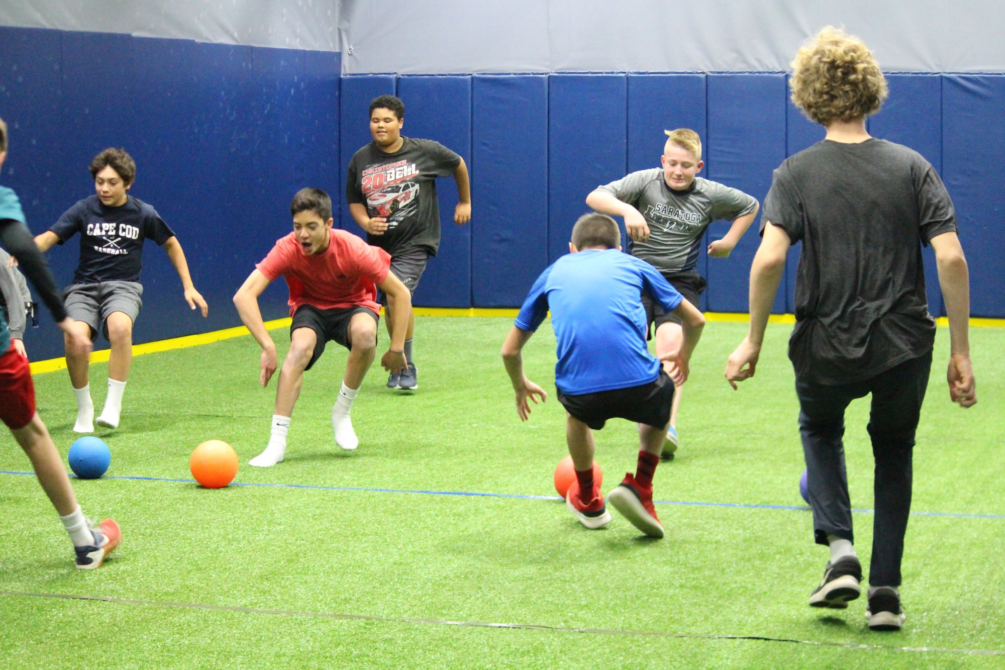 Kids playing dodgeball on the green turf of the Saratoga Sports Club arena